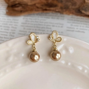 Detail of champagne gold pearl earrings with butterfly studs and crystal accents on ceramic