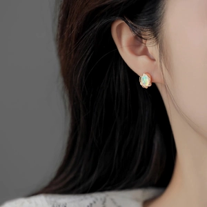 Macro detail of oval opal stud earring with rose gold wavy bezel on model ear