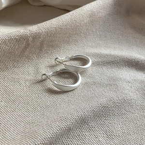 Gros plan de créoles torsadées en argent mat sur un fond en tissu de lin texturé