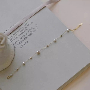 Elegant gold chain bracelet with delicate white pearls and beads on a stylish book