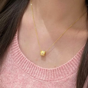 Elegant gold cylinder pendant necklace with pink stones on a pink sweater background