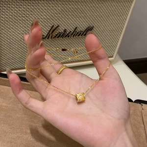 Detail of a gold barrel pendant necklace with pink gems held against a warm background