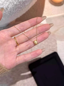 Detail of a gold cylinder pendant necklace and thin hammered ring held by a hand