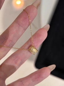 Close-up of gold barrel pendant with matte texture and sparkling stones on thin chain