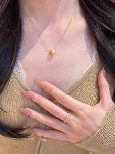 Close-up of a delicate gold barrel pendant necklace and textured ring on a model