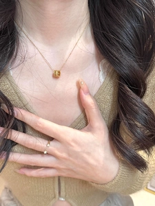 Detail of gold cylinder pendant necklace and floral ring worn on a model in knitwear