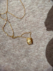Detail of a gold cylinder pendant necklace with sparkling zircon stones on knit fabric