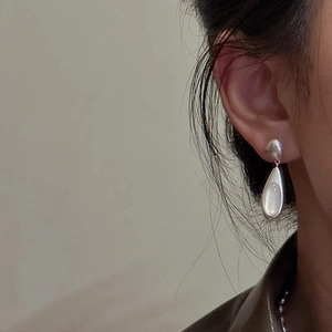 Close-up of teardrop-shaped silver earrings with white gemstone on a model's ear