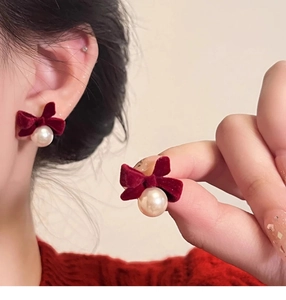 Close-up of red velvet bow earrings with a lustrous white pearl drop on female model