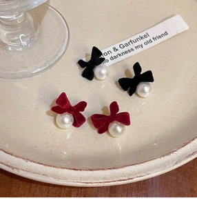 Detail of velvet bow earrings with pearls in red and black on a ceramic tray