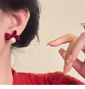 Close-up of velvet wine red bow earrings with hanging pearl on model for autumn style