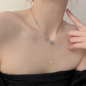 Dettaglio di una catena lunga in argento con anelli geometrici e pendente a cilindro curato