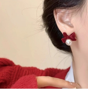 Close-up of red velvet bow earrings with pearl drops worn on ear for festive style