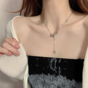 Dettaglio della collana argentata a forma di Y con pendente cilindrico su maglieria