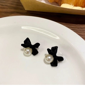 Close-up of elegant black velvet bow earrings with pearl pendants on a ceramic plate