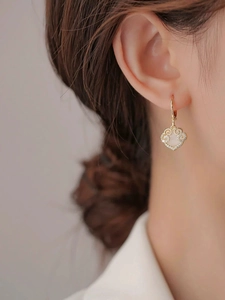 Macro detail of gold earrings featuring ruyi lock design with shell inlay and crystals