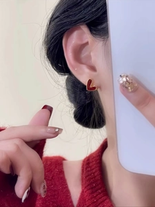Vue détaillée d'une boucle d'oreille cœur rouge avec bords dorés sur un modèle