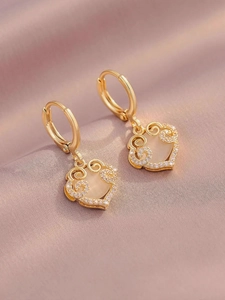 Macro detail of gold-plated hoop earrings with hollow heart charms and cat eye stones