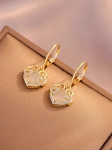Macro detail of gold hoop earrings with heart charms and white opal-like stone inlays