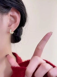 Détail de boucles d'oreilles cœur dorées avec zircons portées sur un pull rouge