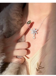 Close-up of snowflake zircon pendant with round pearl on a beige knit sweater