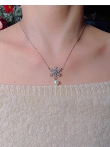 Detail of snowflake zircon pendant with pearl accent worn on a white sweater necklace