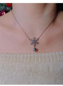 Close-up of snowflake pendant with cubic zirconia and dark gray pearl on a soft sweater