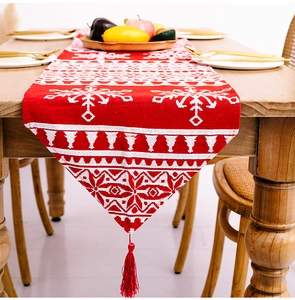 Detailaufnahme eines roten Weihnachtstischläufers mit Schneeflockenmuster und großer Quaste