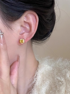 Close-up of square yellow gemstone stud earrings with micro-pave diamond halo on model