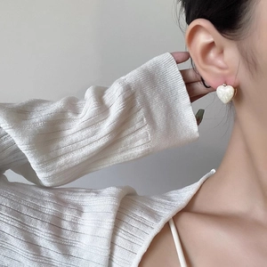 Gros plan de boucles d'oreilles cœur en nacre crème portées avec bordure dorée