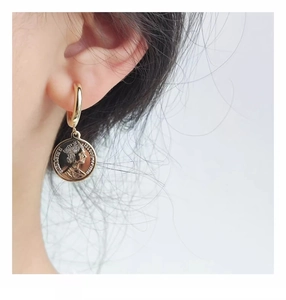 Detail of vintage gold coin drop earrings featuring embossed portrait on white background