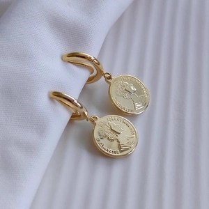 Golden coin earrings with Elizabeth II relief portrait hanging on white fabric