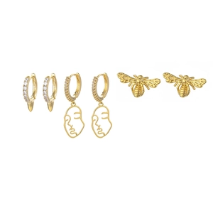 Detailed view of three pairs of gold earrings with bee, abstract face, and cone charms