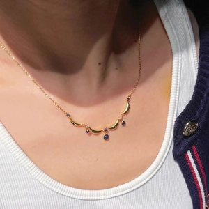 Close-up of vintage gold crescent necklace with dangling navy blue gemstones on a model