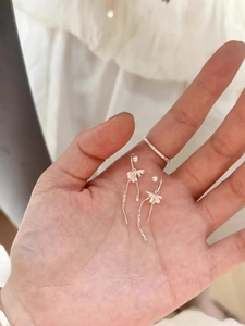 Close-up of silver bow earrings with long tassels and a minimalist diamond ring