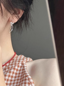Detail of silver ribbon bow earrings and red beaded necklace worn by a female model