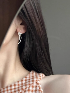 Detail view of silver ribbon bow tassel earrings worn to show elegant drop and movement