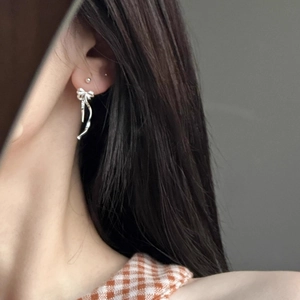 Elegant silver ribbon bow dangle earrings worn by a model in a minimalist setting