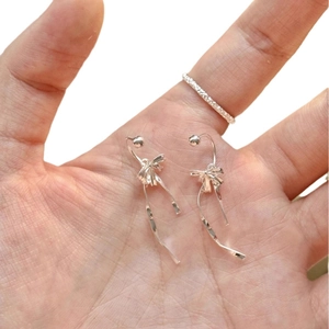 Silver ribbon bow drop earrings with silk-like fluid design held in palm for scale