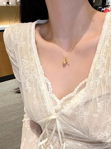 Detailed shot of a gold pinecone pendant necklace with purple zircon on a lace dress