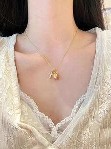 Detail of gold necklace with cross pendant and pink zircon pinecone charm on model