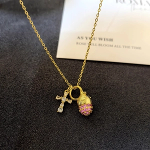Macro shot of gold necklace with silver cross and pink crystal pinecone pendant