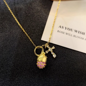 Detailed shot of gold necklace with pink zircon pomegranate and small cross charms