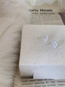 Macro detail of silver floral C-shape stud earrings with three flowers on gift box