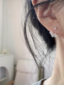 Detail view of silver floral cluster earrings and small stud on model's ear
