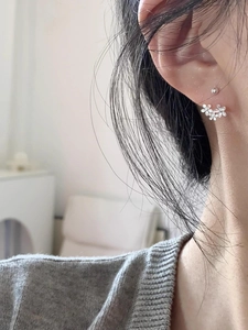 Close-up of small floral silver earrings worn by a model in a natural setting