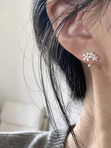 Detail of silver floral stud earrings featuring three blossoms worn on a model's ear