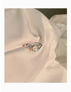 Close-up of S-shaped silver ring featuring a spherical iridescent gemstone on silk