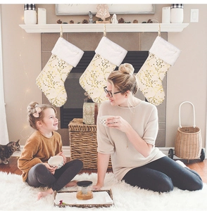 Three plush cream Christmas stockings with gold branch patterns by a cozy fireplace