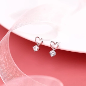 Détail de boucles d'oreilles cœur en argent avec zircone sur un tissu de soie rose doux